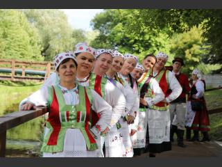 Zespół kobiet w strojach ludowych na kładce na rzece Orzysz. Pozują do wspólnego zdjęcia.