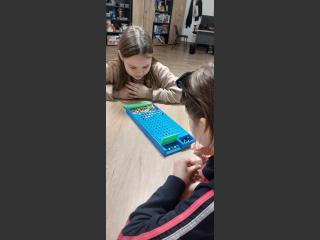 Dwie dziewczynki siedzą przy stole i grają w grę "łamacz kodów".