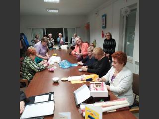 W Pawilonie Sosnowym, przy stole kobiety z Klubu Seniora szyją.