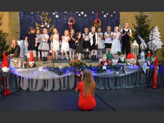Na scenie dzieci z zespołu Neonutki, występ Bożonarodzeniowy. Scena ozdobiona w motywy świąteczne, lapmki choinkowe, wieńce bożonarodzeniowe, gwazdki 