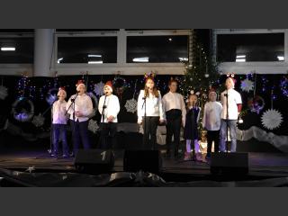 8 dzieci śpiewających na scenie,w czapkach Mikołaja.