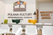 Sala w bibliotece polany Kultury. Duży stół, krzesla, na ścianie logo Polany Kultury.
