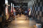 Kobiety z zespołu Orzyszanki w studiu nagrań. Przed nimi statywy mikrofonowe, z tyłu perkusja. 
