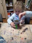 Dziewczynka siedzi przy stole, trzyma w rękach pomalowane przez siebie plastikowe kubki.
