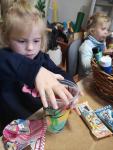 Dwie dziewczynki przy stole, w rękach mają pomalowane prze siebie kolorowe kubki. 