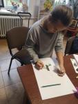 Dziewczynka maluje na kartce kaczkę podczas zajęc plastycznych na Polanie Kultury.