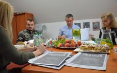 Organizatorzy  	II Przegląd Piosenki Patriotycznej i Żołnierskiej o statuetkę Tytanowego Tygrysa, siedzą przy stoliku, rozmawiają. Na stole dyplomy, owoce, ciastka.