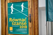 Plakat "Równać Szanse" na drzwiach w budynku Polany Kultury w Orzyszu