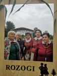 Kobiety z zespołu Orzyszaki w strojach ludowych pozują do zdjęcia w ramce z napisem ROZOGI