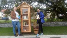 Dwie osoby pozują do zdjęcia z domkiem z książkami