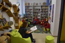 Dzieci słuchają czytanej przez bibliotekarkę książki