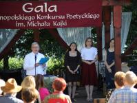Na scenie z prawej strony laureatki Ogólnopolskoego Konkursu Poetyckiego im. Michała Kajki. Z lewej strony mężczyna, przed nim statyw mikrofonowy.