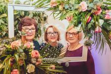 Trzy kobiety pobujące do zdjęcia w ramie ozdobionej kwiatami.