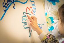 Dziewczynka robi odcisk palca pomalowanego niebieską farbą na obrazie z dłońmi.