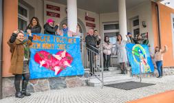 Pracownicy MOPSu pozują do zdjęcia z transparentami rozwieszonymi przy wejściu do Ratusza w Orzyszu. Na transparencie z lewej strony serce i dłonie, na transparencie z prawej strony kula ziemska.