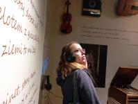 Kobieta ze sluchawkami w Muzeum. Za nią na ścianie instrumenty, cytaty.