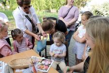 Dzieci zebrane dookoła stanowiska z malowaniem twarzy. Radna Pani Halina Mikucka częstuje dzieci słodyczami.