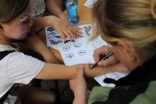 Kobieta maluje na ręce dziewczynki zmywalny tatuaż - serduszko. Na stole leżą wzory tatuaży.