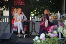 Na scenie na krześle Pani Dyrektor Polany Kultury- Joanna Kamieniecka, na kanapie Laura Łącz. W tle drzewa.