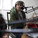 Dziewczyna w studiu Radia Orzysz, ma słuchawki, przed nia statyw mikrofonowy 