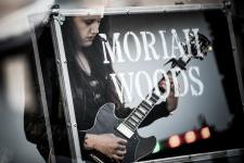 Napis Moriah Woods. Kobieta gra na gitarze podczas majówkowego koncertu.