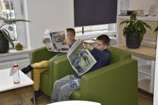 Chłopcy siedzą w fotelach i czytają gazety