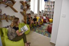 Dzieci siedzą na pufach gdy bibliotekarka czyta im książkę 