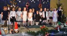 Na scenie dzieci z zespołu Neonutki, występ Bożonarodzeniowy. Scena ozdobiona w motywy świąteczne, lapmki choinkowe, wieńce bożonarodzeniowe, gwazdki