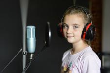 Dziewczynka ze słuchawkami na uszach, przed nią mikrofon
