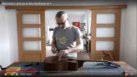 Krzysztof Roszko w pracowni lutniczej, przed nim na stole leży gitara akustyczna. Podczas wymiany strun w gitarze.