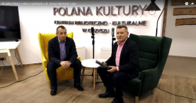 Dwóch mężczyzn siedzi na fotelach. Za nimi Logo Polany Kultury. W bibliotece Polany Kultury.