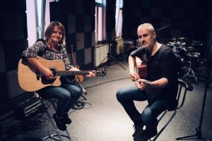 W studiu nagrań. Z lewej strony kobieta trzyma gitarę, z prawej strony Krzysztof Roszko trzyma gitarę.